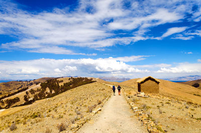 Rear view of hikers walking on dirt road at isla del sol against sky