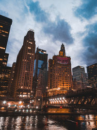 Illuminated buildings by river against sky in city