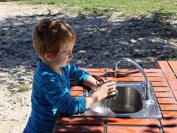 A six-year-old boy washes a dish sponge in the sink in an open kitchen.