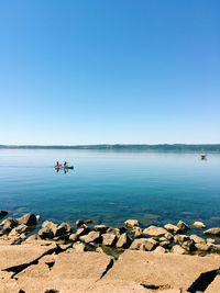 Distance view of people kayaking in lake against clear sky