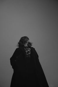 Low angle view of young woman standing against gray background