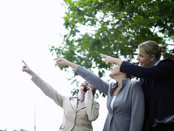 Smiling businesswoman with colleagues pointing against sky