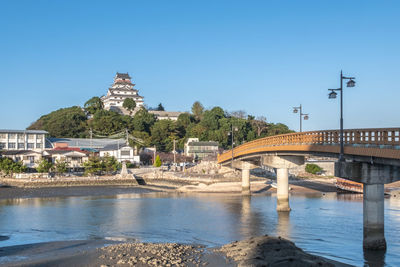 Arch bridge over river by buildings against clear blue sky