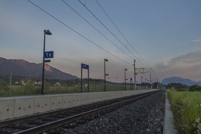 Railroad tracks by road against sky during sunset