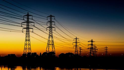 Silhouette electricity pylon against orange sky