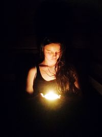 Close-up of woman with illuminated light bulb against black background