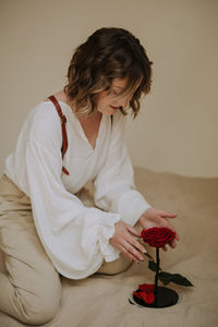 Young female in victorian shirt sitting with rose on the sand and smile