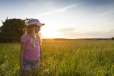 Woman standing on field against sky during sunset