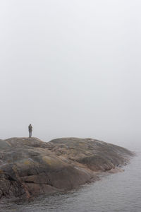 Man standing on rock by sea against sky