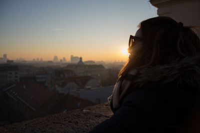 Woman in city against sky during sunset