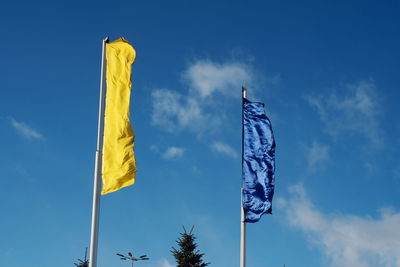 Two flags, yellow and blue, flutter in the wind across the sky on a sunny day.