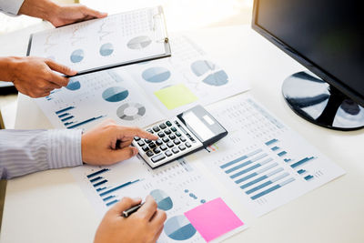 Midsection of businessman using calculator while colleague holding clipboard table in office