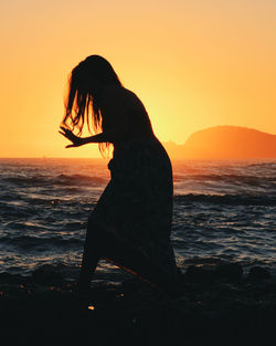 Silhouette woman on beach against sky during sunset