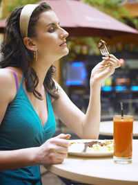 Side view of woman having food while sitting at sidewalk cafe