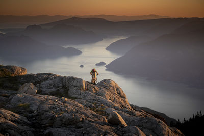 Man on rock by mountain against sky during sunset