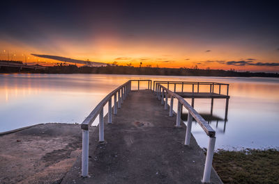 Pier over river against sky during sunset