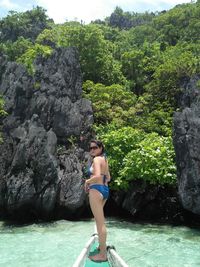 Full length of young woman standing on rock against trees