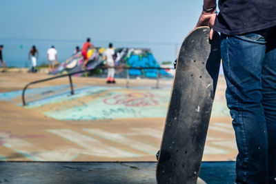 Midsection of man holding skateboard at park against clear sky