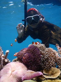 Snorkeling wearing a hijab in the clear ocean wearing a snorkel set and greeting nemo fish