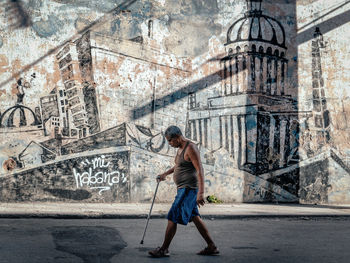 Full length of man holding umbrella on street against building in city