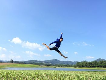 Low angle view of woman jumping on field against sky