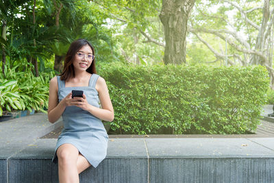 Smiling young woman using mobile phone while sitting on tree