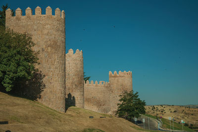 Lined stone towers on the large city wall in romanesque style next to street, in avila, spain.