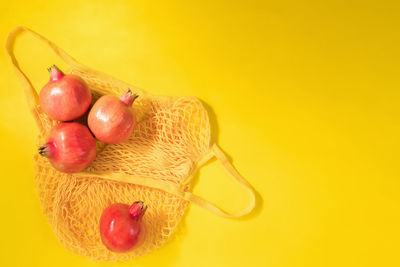 Fresh ripe pomegranate in eco cotton net or mesh shopping bag on yellow background