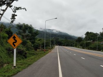 Road sign by trees against sky