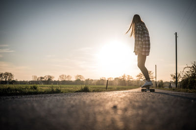 Full length of woman skateboarding on road against sky