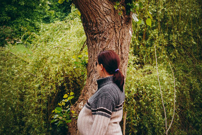 Side view of woman standing by tree trunk