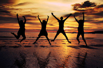 Silhouette friends jumping at beach during sunset