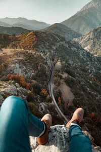 Low section of man sitting on cliff against mountains