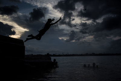 Silhouette of jumping in sea against sky