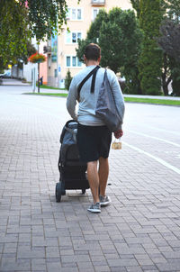 Man walking and pushing a baby stroller in city carrying reusable grocery bag and white face mask