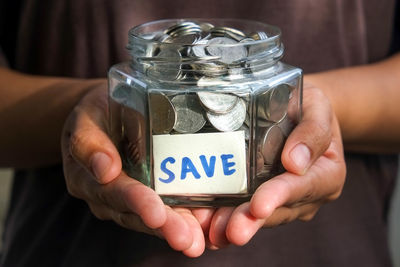 Close-up of human hand holding jar with save label and coins