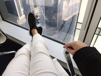 Low section of person sitting by glass window on chair