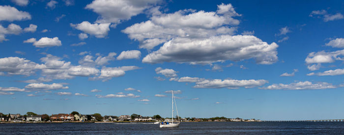 A sailboat in the great south bay with very blue sky and thick puffy white clouds above.