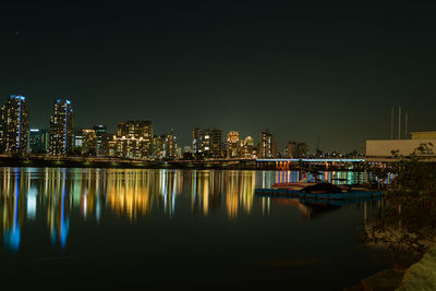 Illuminated buildings by river against sky at night