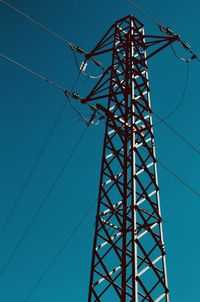 Low angle view of electricity pylon against blue sky