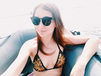 Portrait of beautiful woman wearing bikini top while sitting in inflatable raft on sea during sunny day