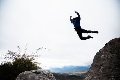 Man jumping on rock against sky