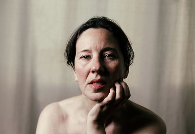 Portrait of shirtless mature woman with hand on chin against curtain at home