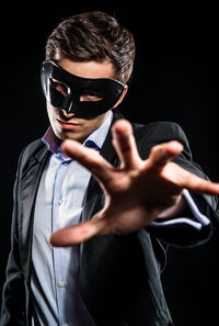 Portrait of man in mask gesturing while standing against black background