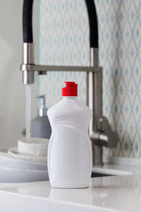 A white bottle with dishwashing gel on the background of a sink with dirty dishes 