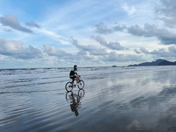 Man riding bicycle on sea against sky