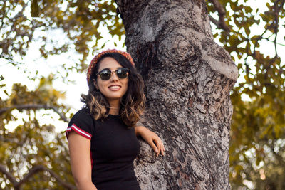 Portrait of a smiling young woman against tree trunk