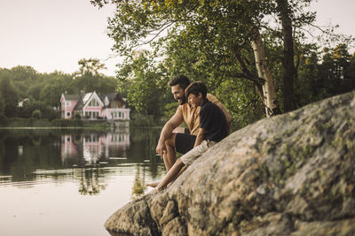 Father and son sitting on rock near lake