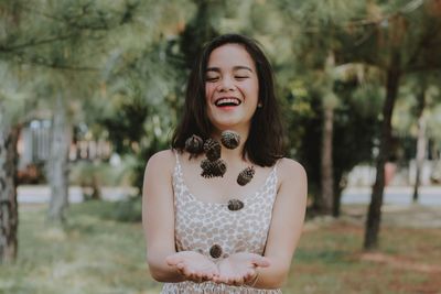 Beautiful woman tossing pine cone in air standing in park