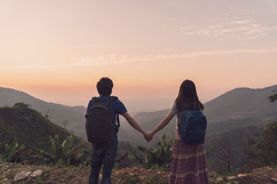 Rear view of friends standing on mountain against sky during sunset